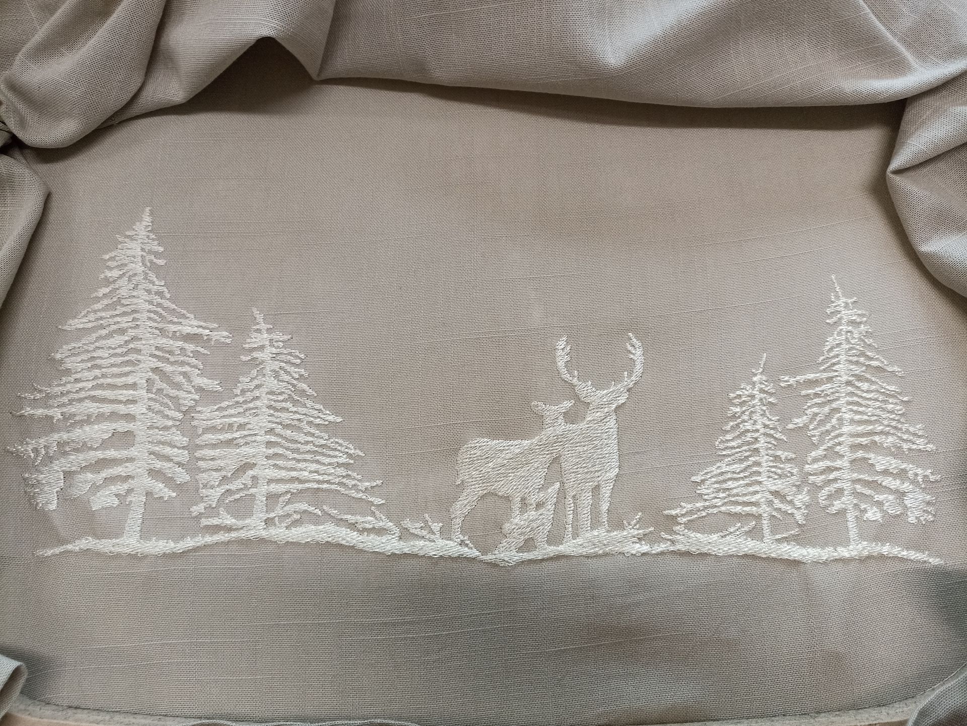 Primo piano di una coperta con ricamati un cervo e degli alberi.