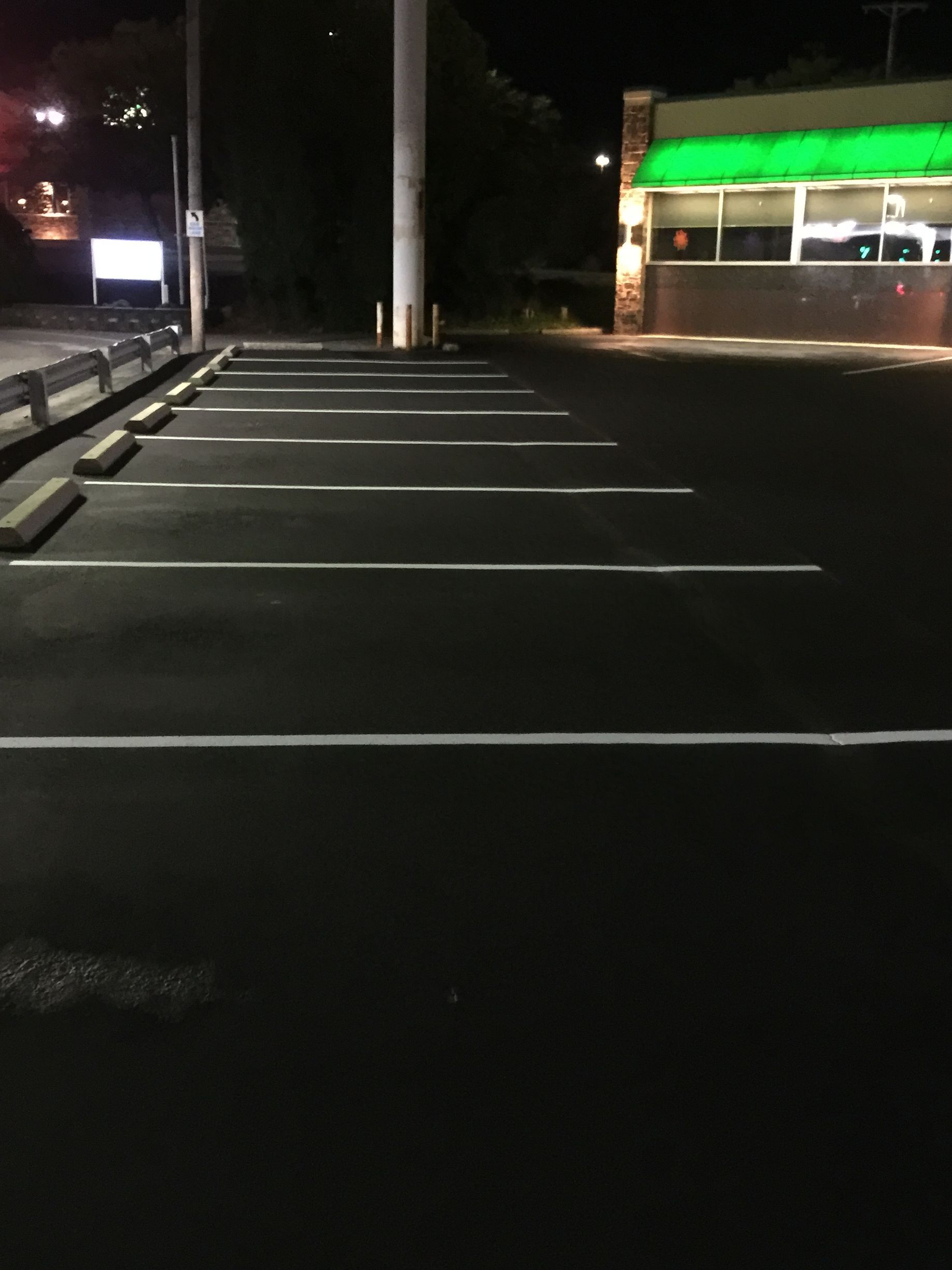A parking lot with a green building in the background at night.