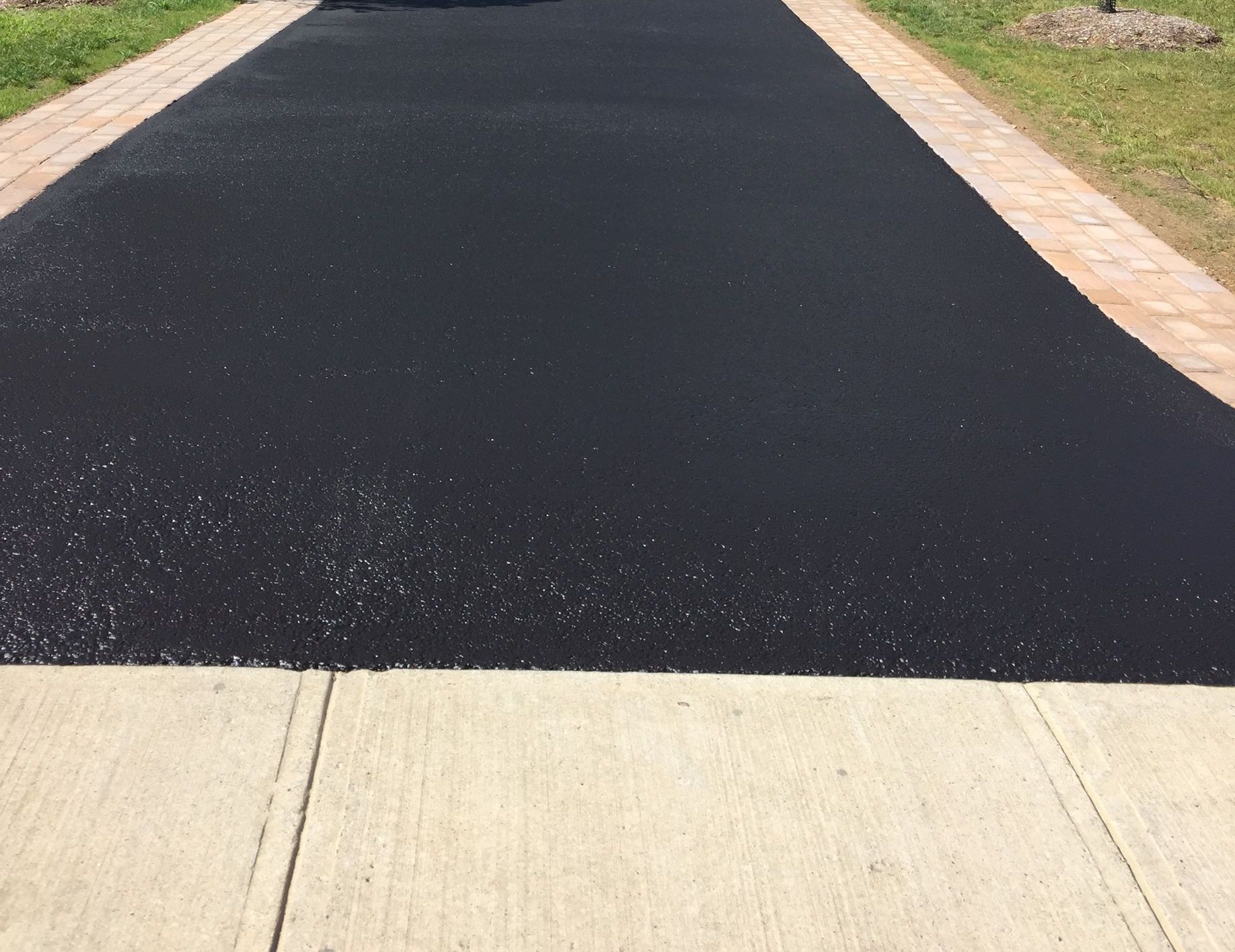 A black asphalt driveway with a brick curb