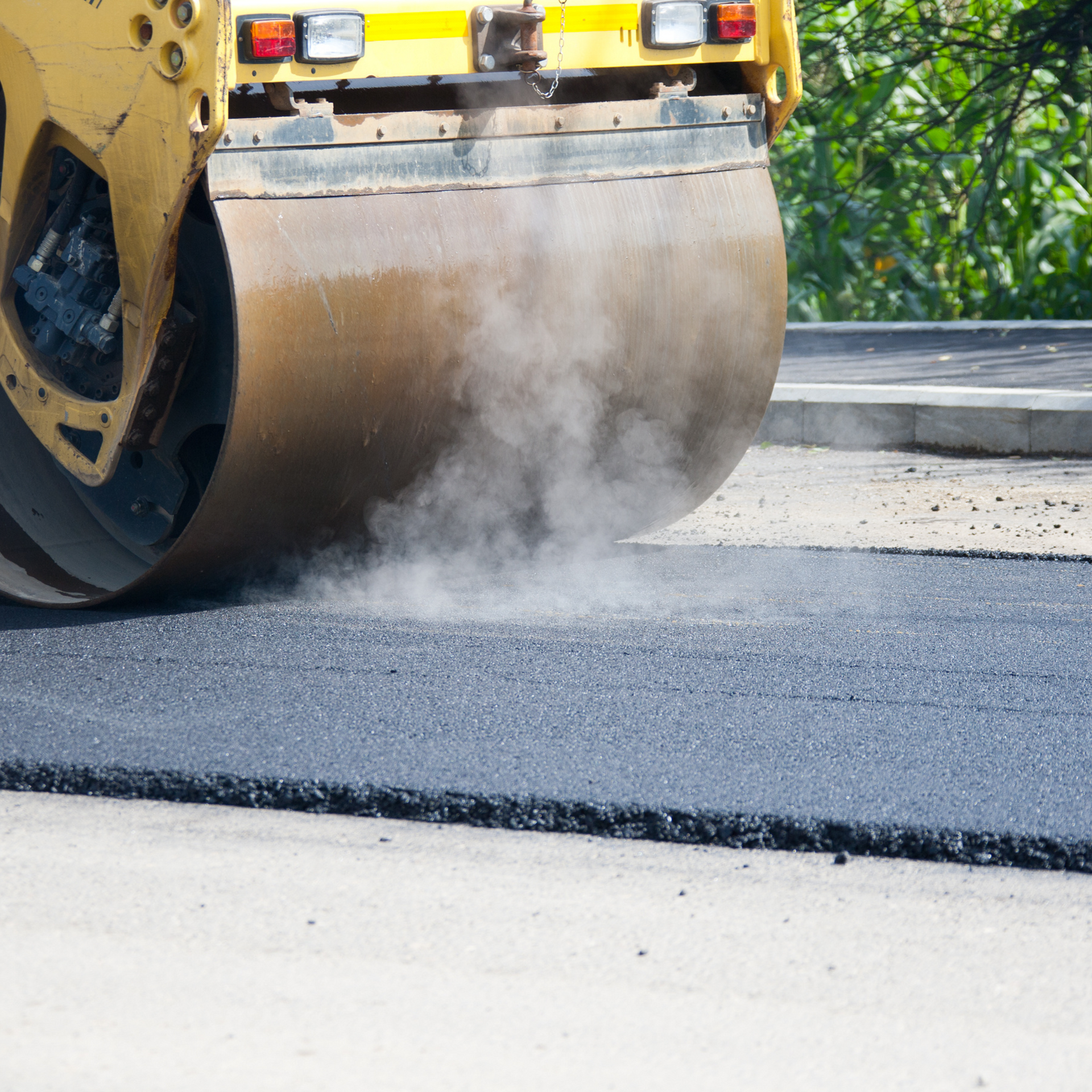 A yellow roller is rolling asphalt on a road