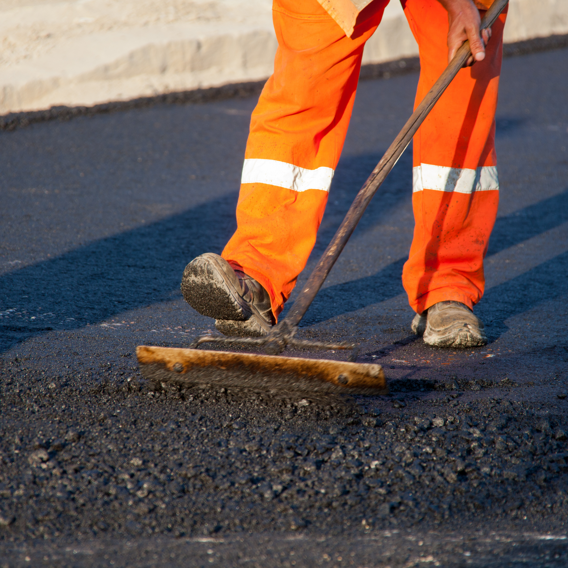 A man in orange pants is using a paver to spread asphalt