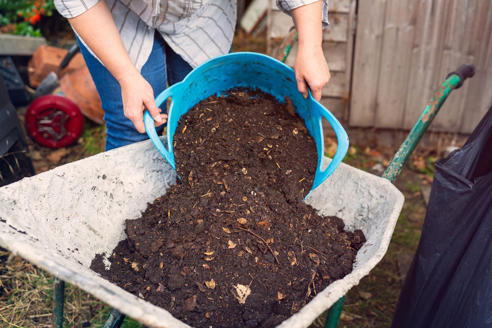 Woman adding compost to a wheelbarrow, supporting sustainable soil supplies for gardening.