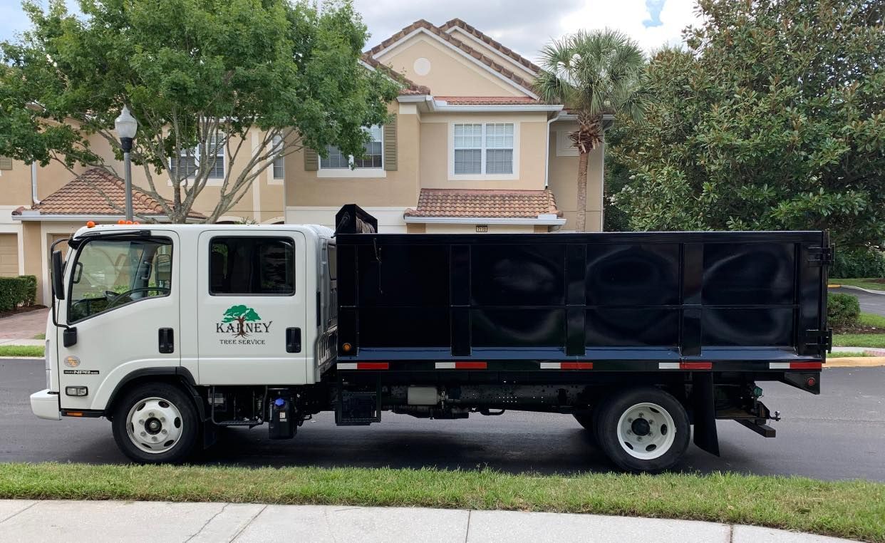 White and black landscaping truck parked on the side of the road in front of a tan building.