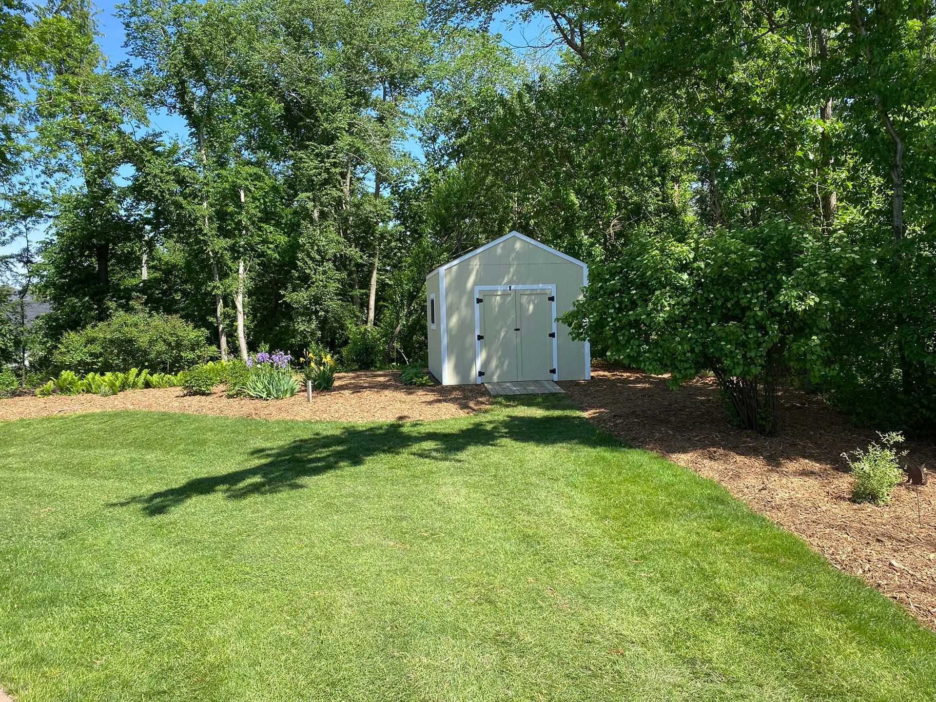 A white shed is sitting in the middle of a lush green field.