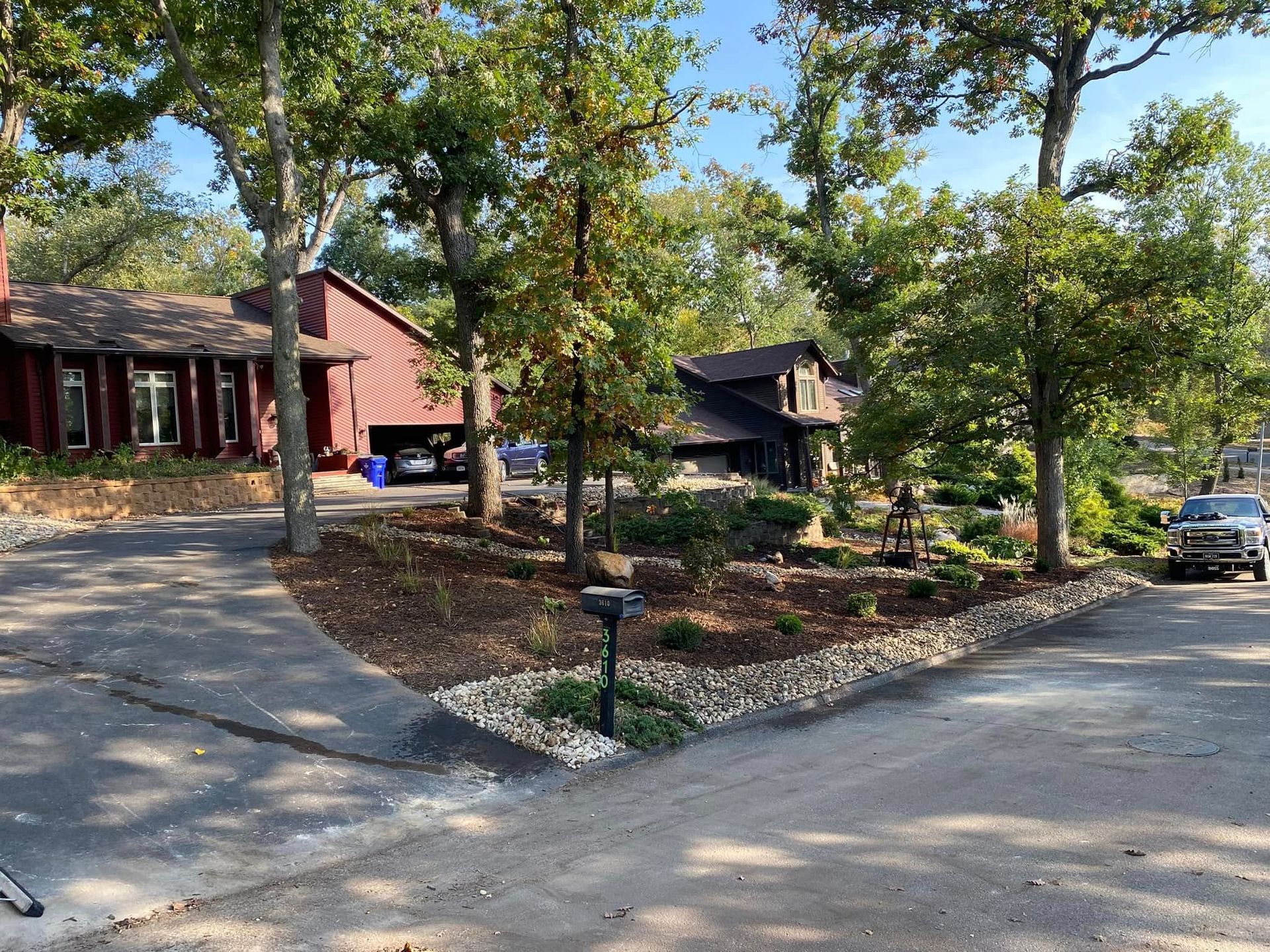 A car is parked on the side of the road in front of a house surrounded by trees.