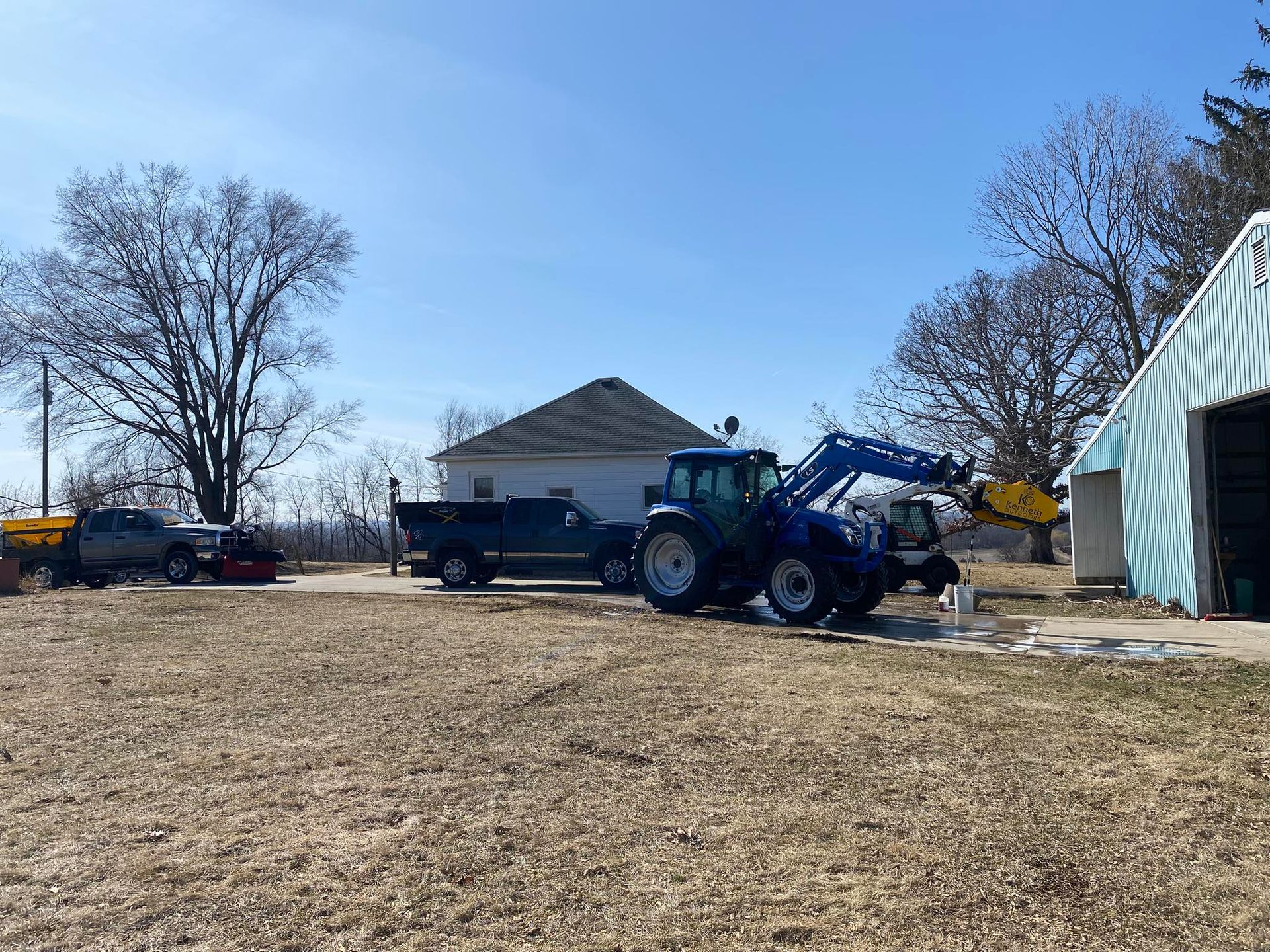 A blue tractor is parked in a field in front of a house.