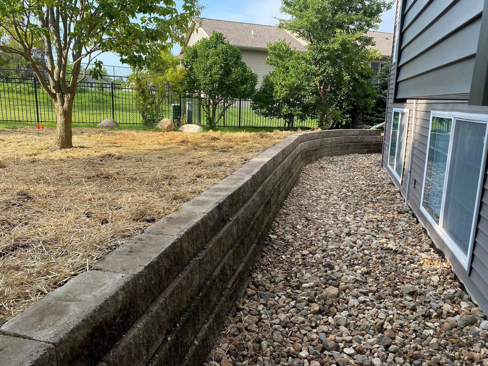 A house with a stone wall and gravel in front of it.
