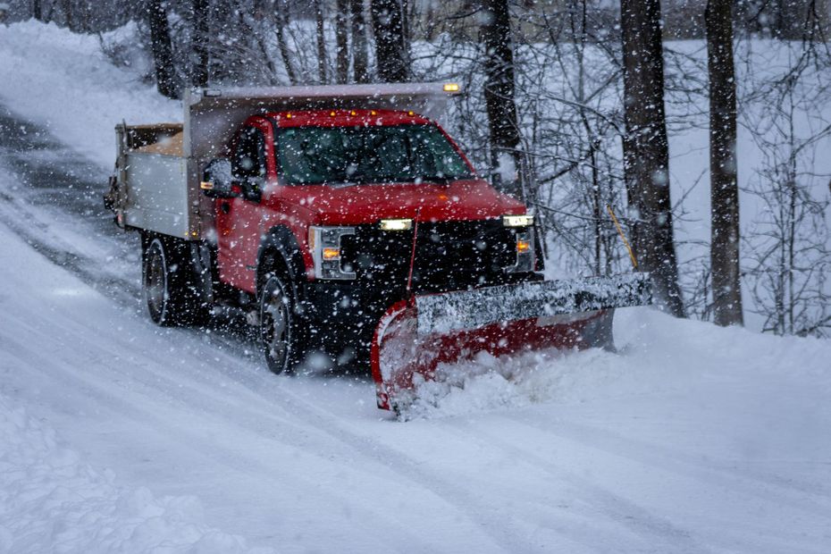 A red truck is plowing snow on a snowy road.