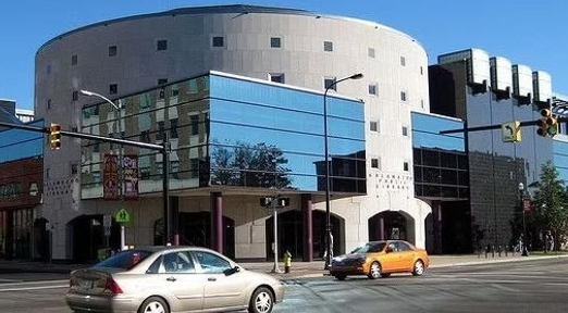 A car is driving down a street in front of a large building