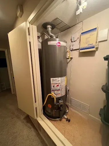 A Rheem water heater in a closet with a vent and access panel.