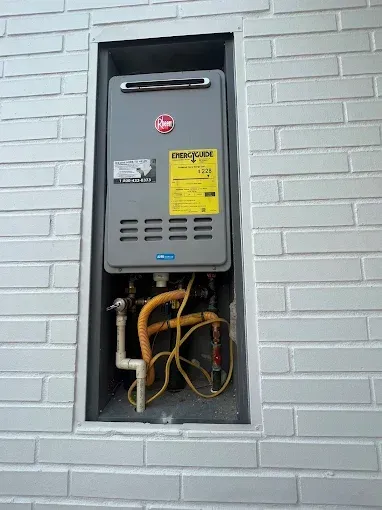 Rheem tankless water heater installed in an exterior brick wall alcove.