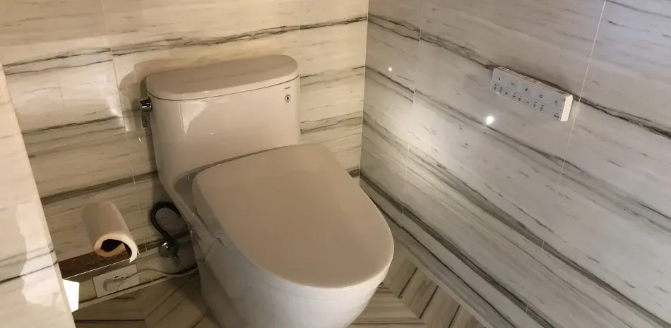 A modern white toilet in a bathroom with marbled walls and floor.