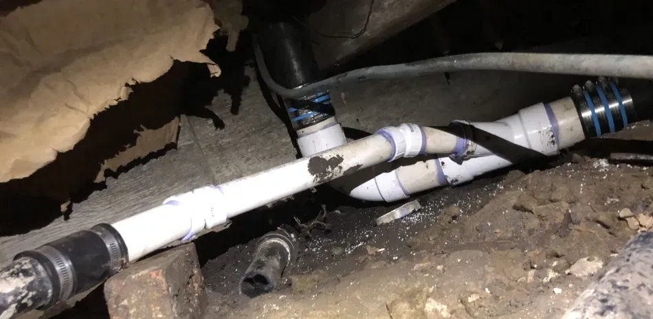 Plumbing pipes with a Y-connection, black tape, and clamps in a confined space.