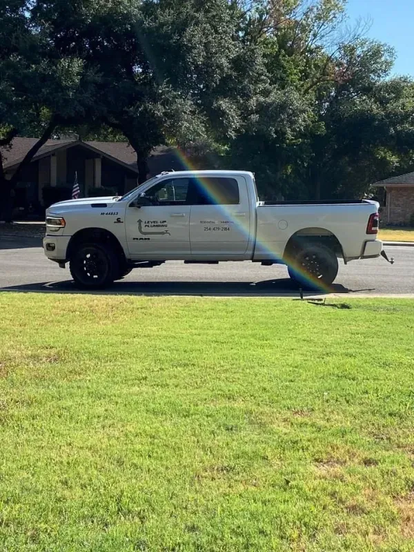 White pickup truck parked on a street with green grass. Rainbow appears in the background.