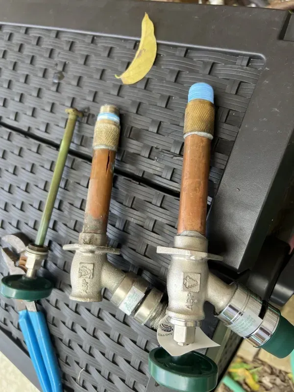 Two copper pipes with valves, blue caps, and green handles, on a black surface.