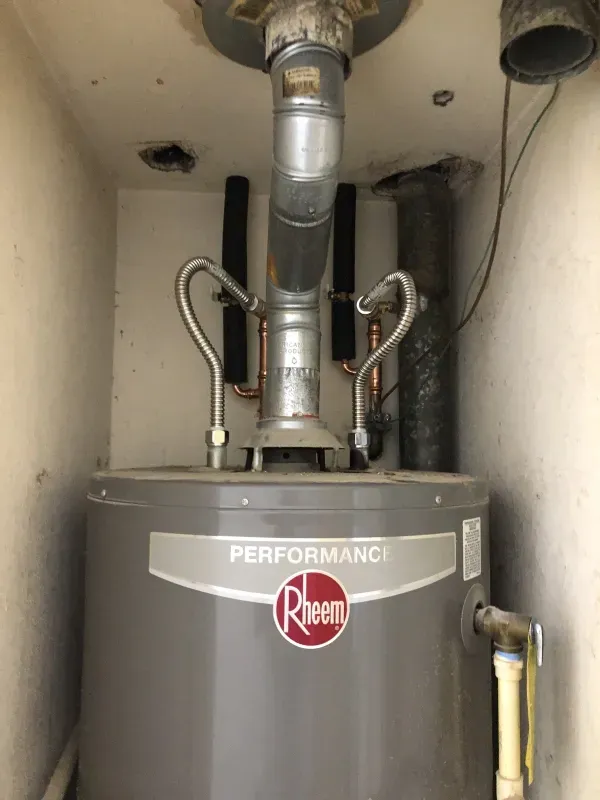 Rheem Performance water heater in a utility closet with vent pipes and copper plumbing.