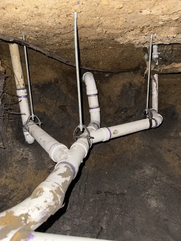 White PVC plumbing pipes branching out, suspended from a dark, rough ceiling.
