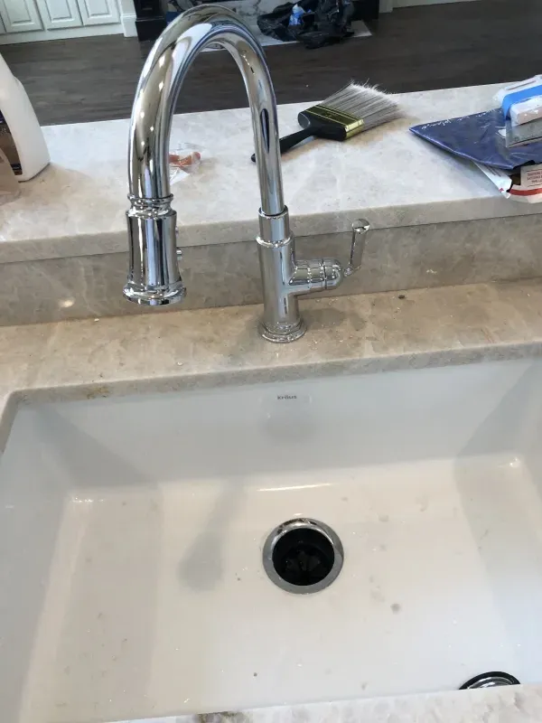 A chrome kitchen faucet over a white sink. Construction tools and supplies are nearby.