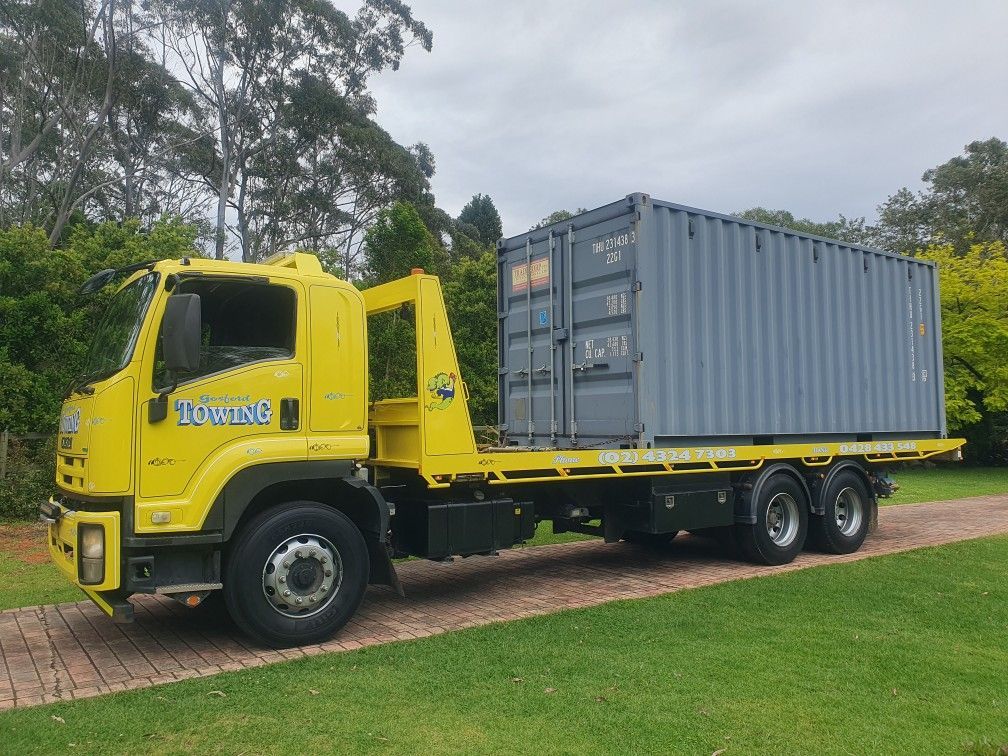 A yellow tow truck is carrying a container on the back of it.