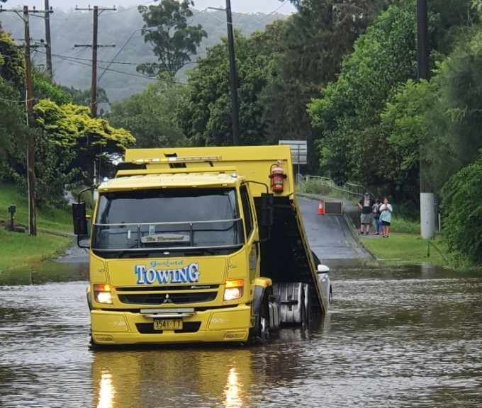 A yellow towing truck is driving through a flooded road