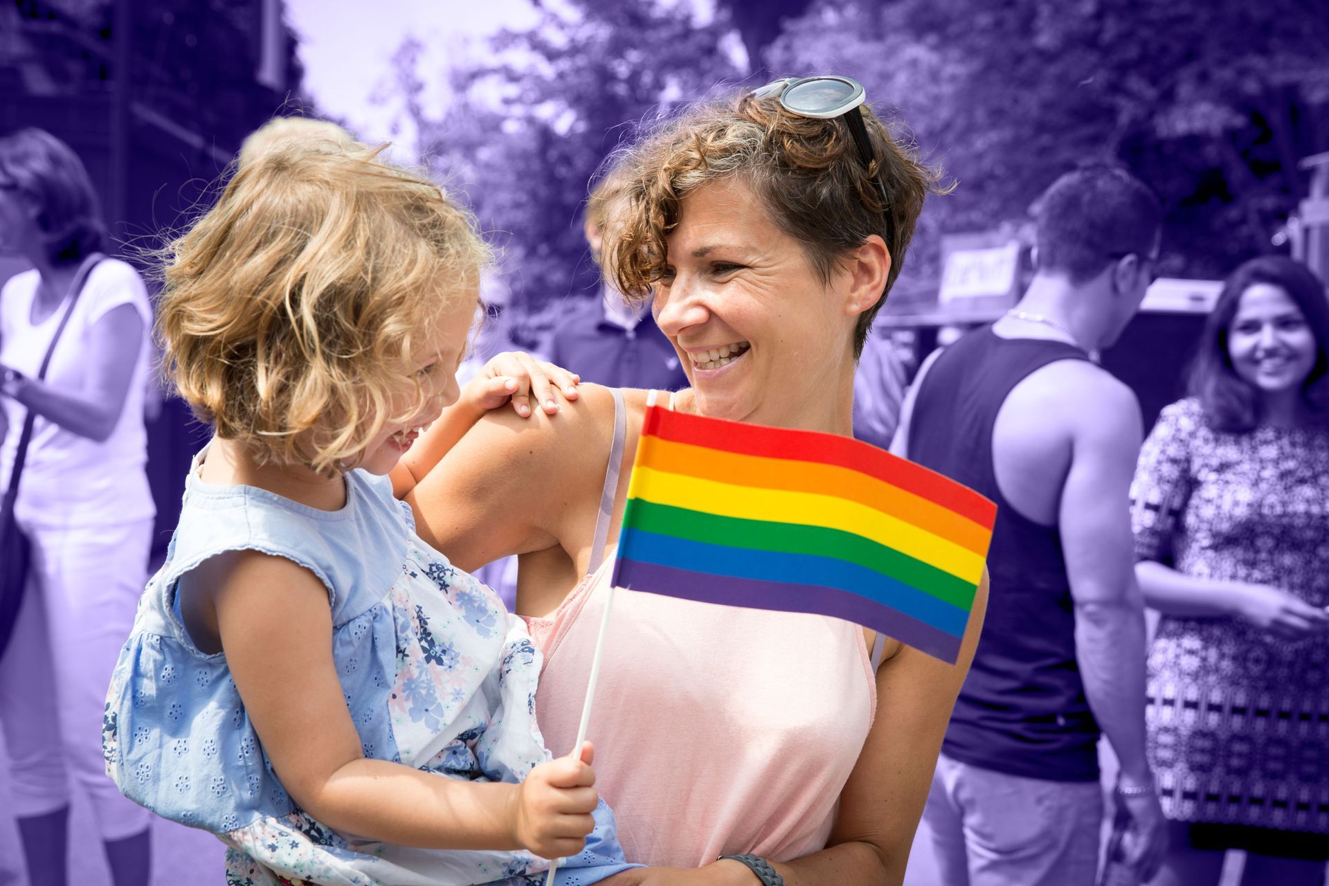 Mãe com uma criança, segurando a bandeira do orgulho LGBTQIA+, no colo.