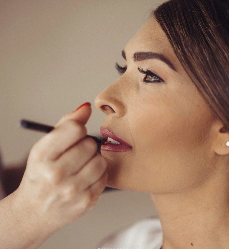 Donna che si fa truccare gli occhi, riflessa in uno specchio, con la tavolozza del trucco in primo piano.