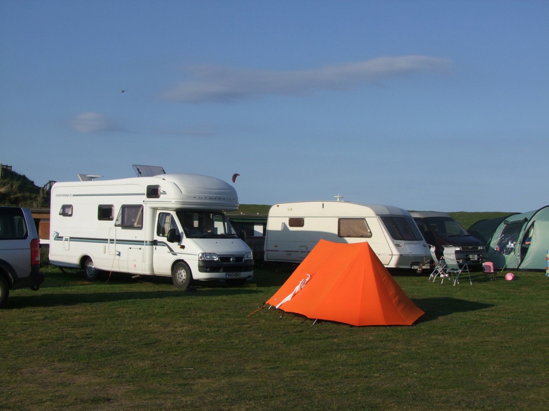 A row of camper vans are parked in a grassy field