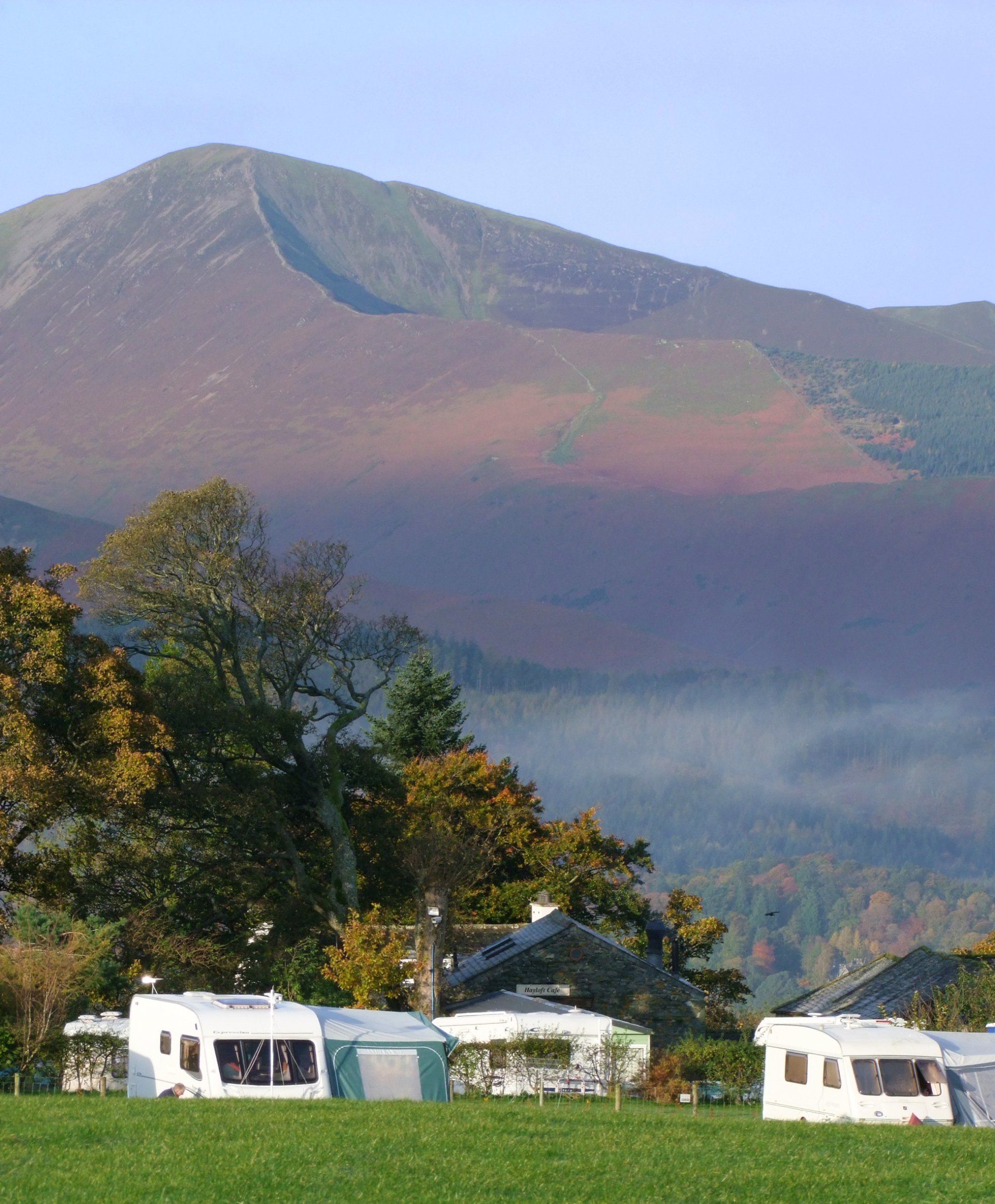 A row of caravans are parked in a field with a mountain in the background