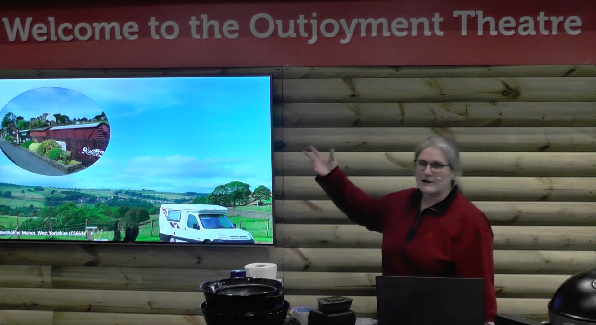 A woman stands in front of a screen that says welcome to the outjoyment theatre