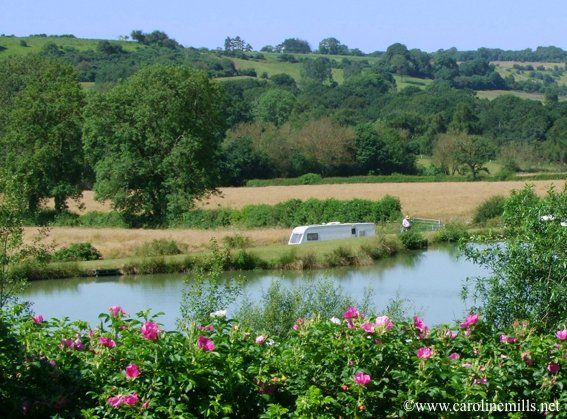 A white caravan is parked on the shore of a lake at a campsite