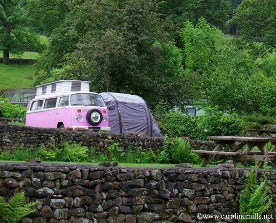 A pink VW retro campervan is parked in front of a stone wall
