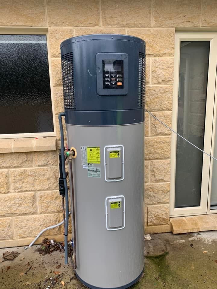 Heat pump water heater against a brick wall, with digital control panel.