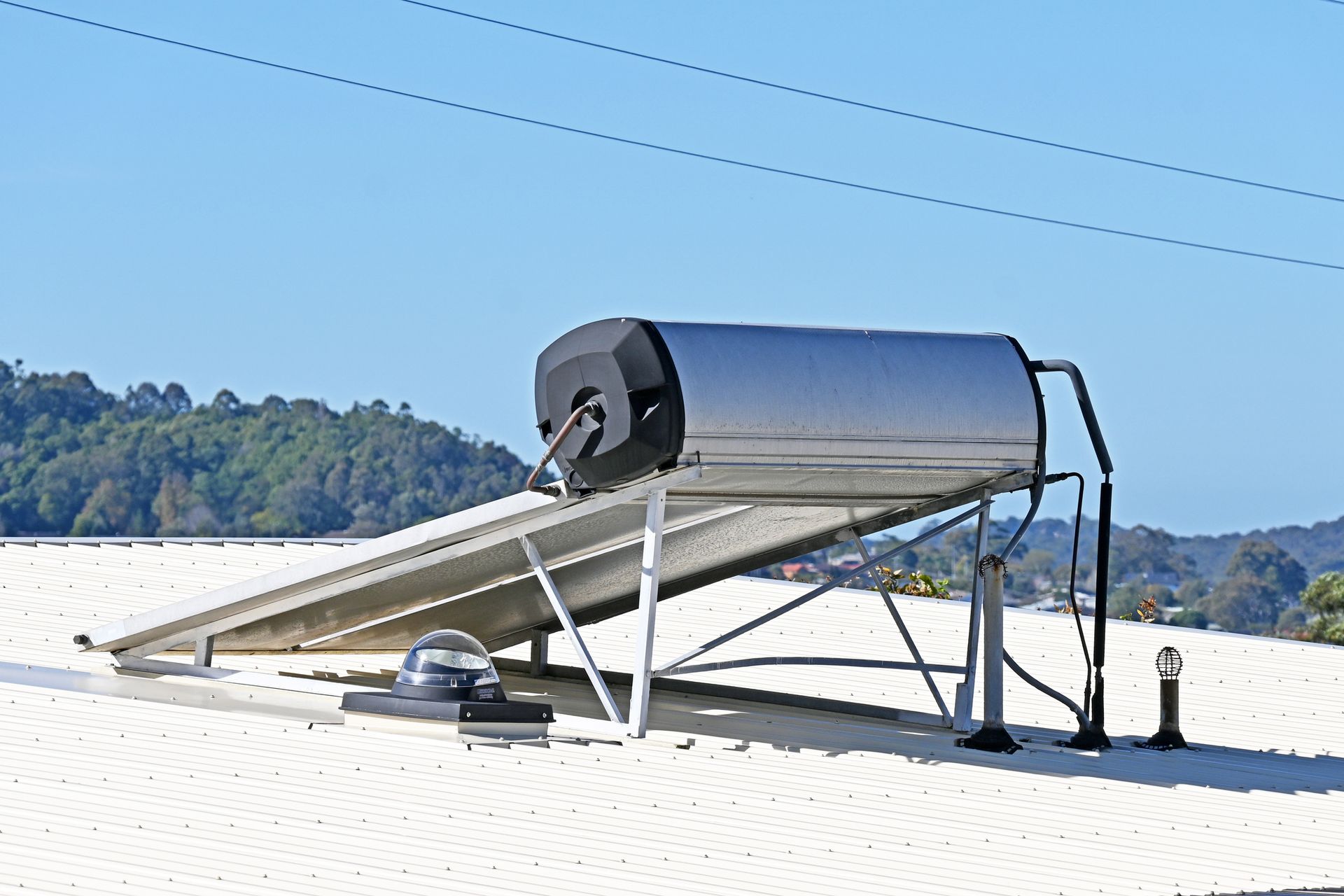 Solar panels, water heater, and power lines on a rooftop under a bright blue sky.