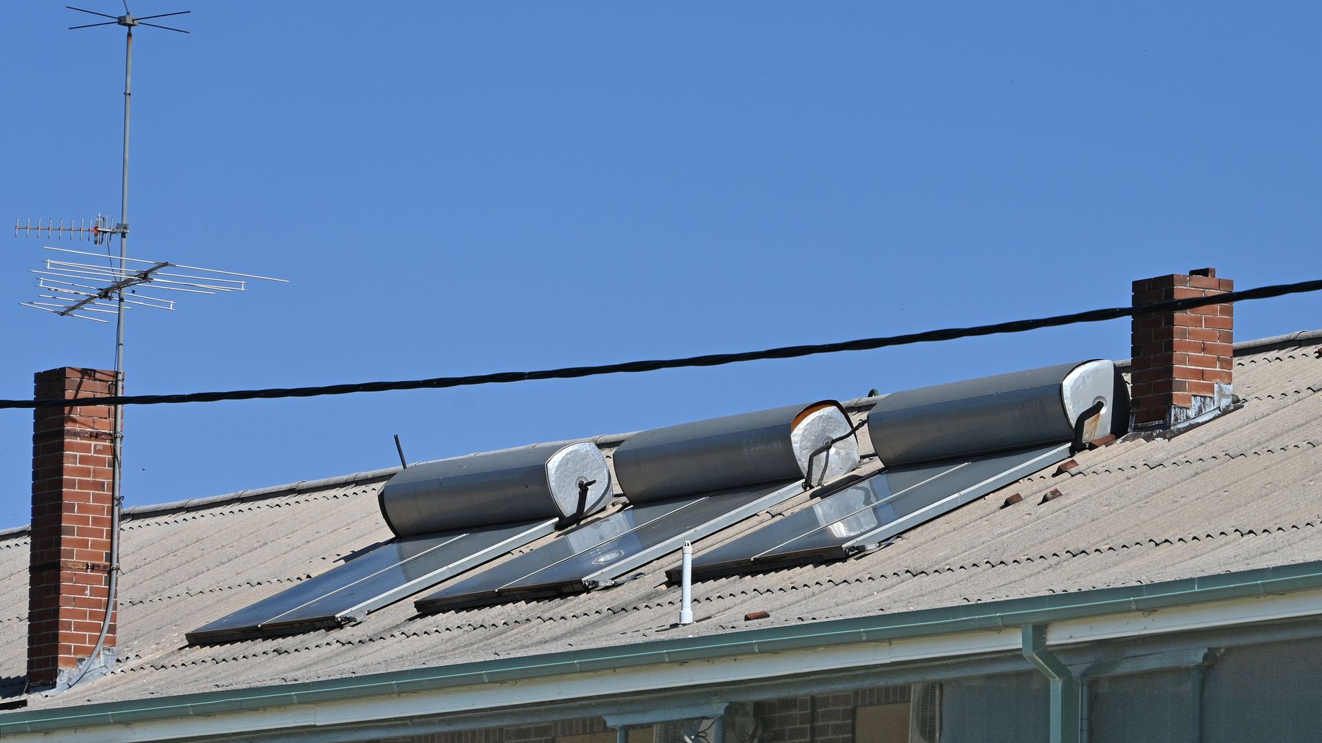 Solar water heaters on a rooftop with antennas and a brick chimney against a blue sky.