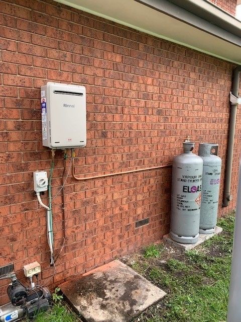 Yellow-handled valve on corroded copper pipe in front of a brick wall.