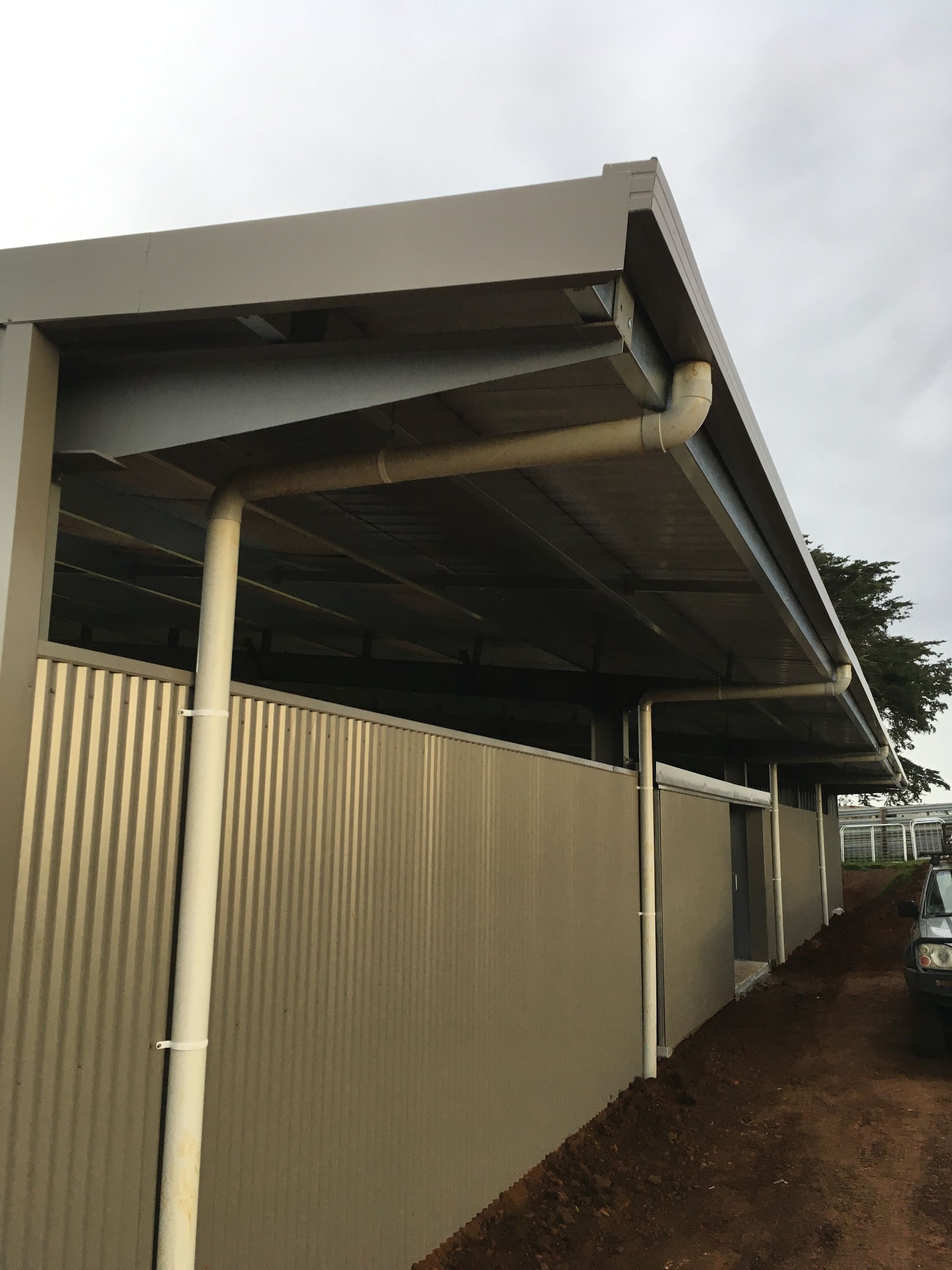 Person installing a black gutter with a drill on a house with blue siding.