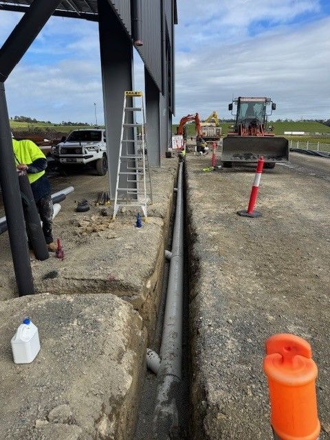 A gray and white heat pump water heater against a brick wall, next to a power outlet.