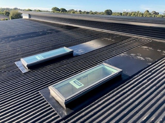 Workers on a rooftop installing corrugated metal panels, against a building and blue sky.