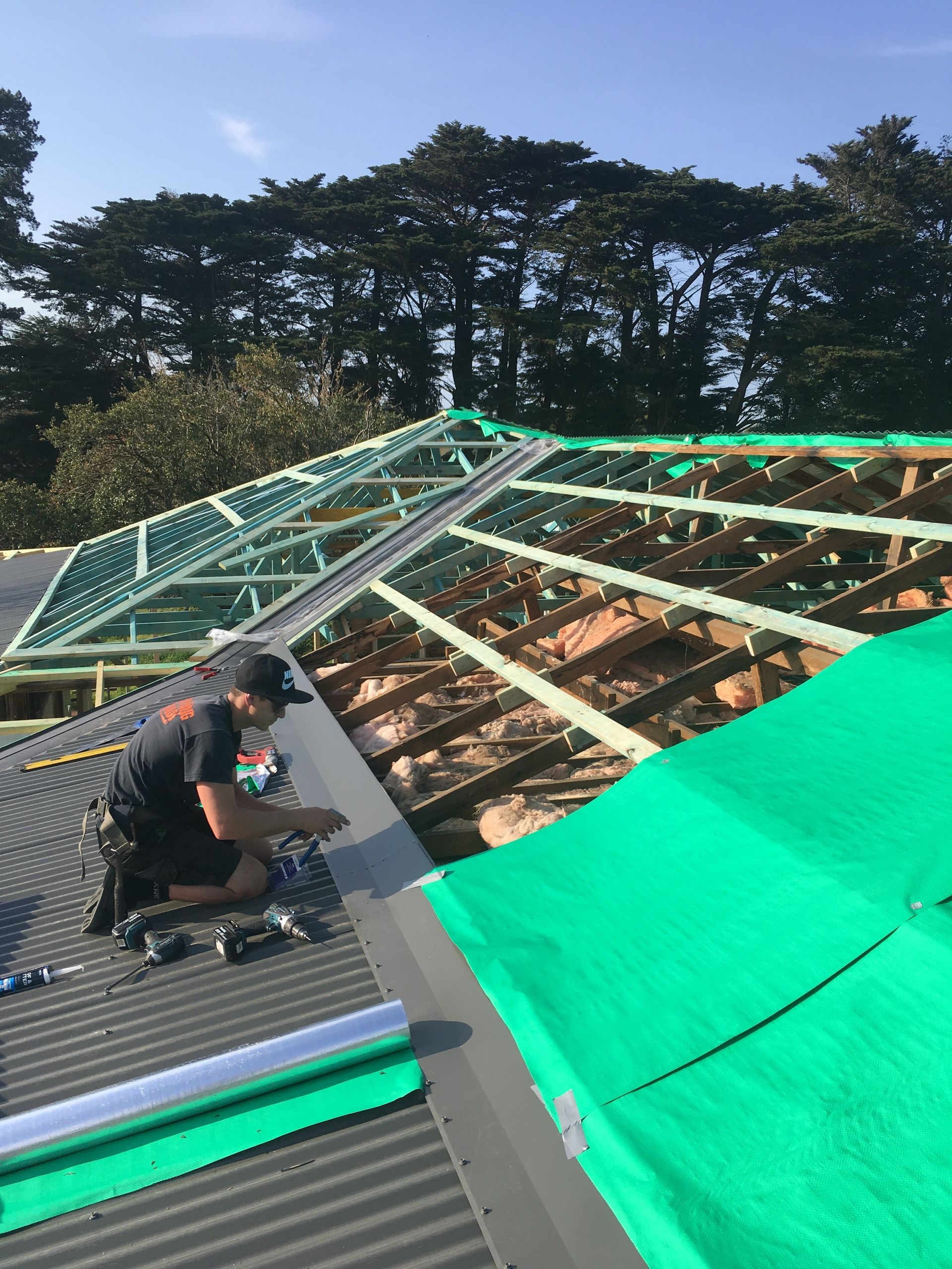 Workers installing a white corrugated metal roof on a building under a blue sky.