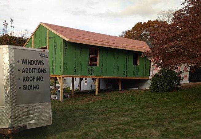 A house is being built with green siding and a sign that says windows additions roofing siding.