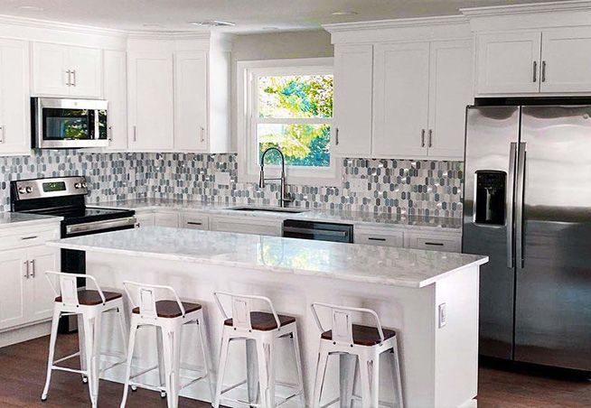 A kitchen with white cabinets , stainless steel appliances , and a large island.