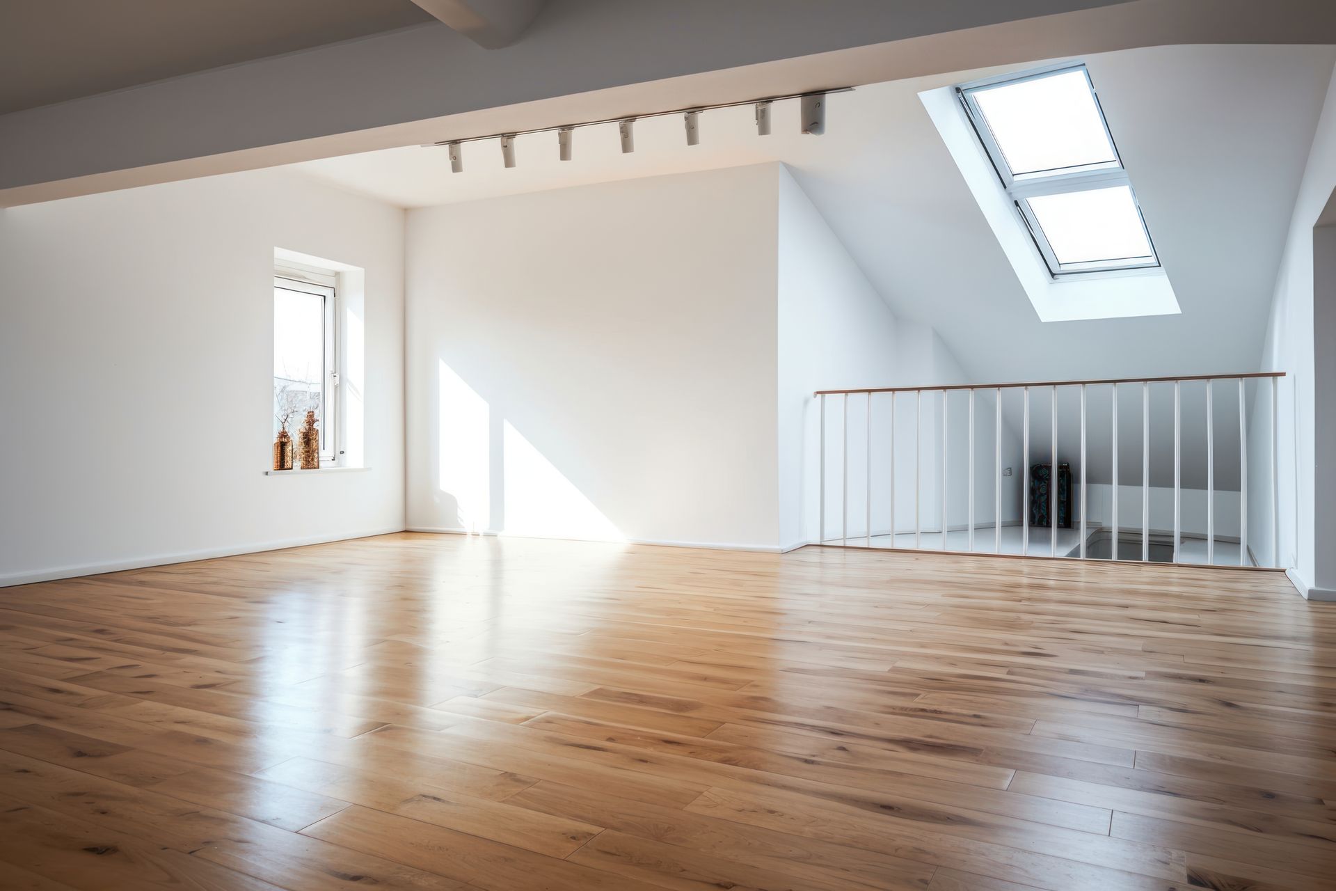 An empty room with hardwood floors and a skylight in the ceiling.