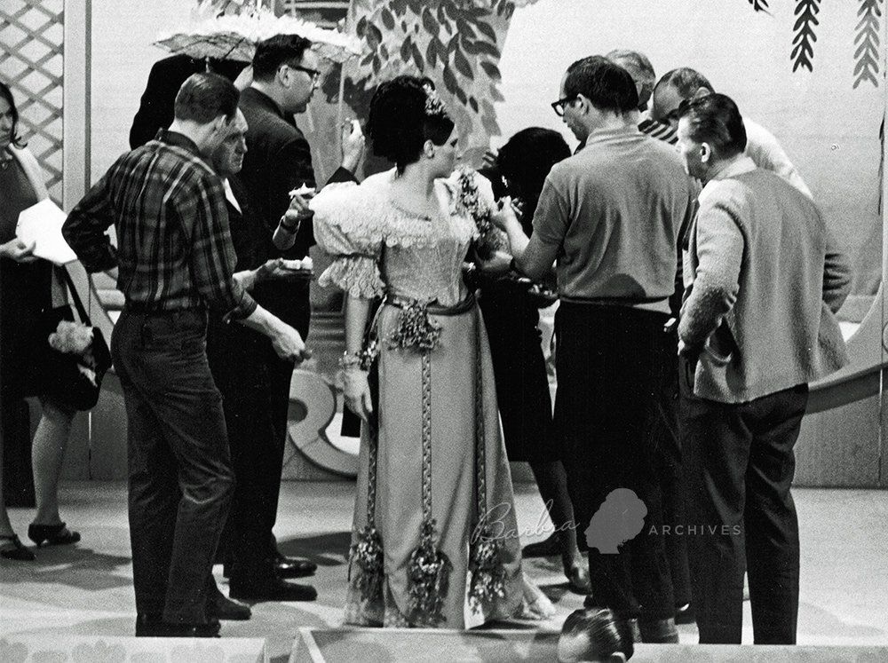The TV crew gathered around Barbra Streisand, rigging her gown to rip away for the cameras.