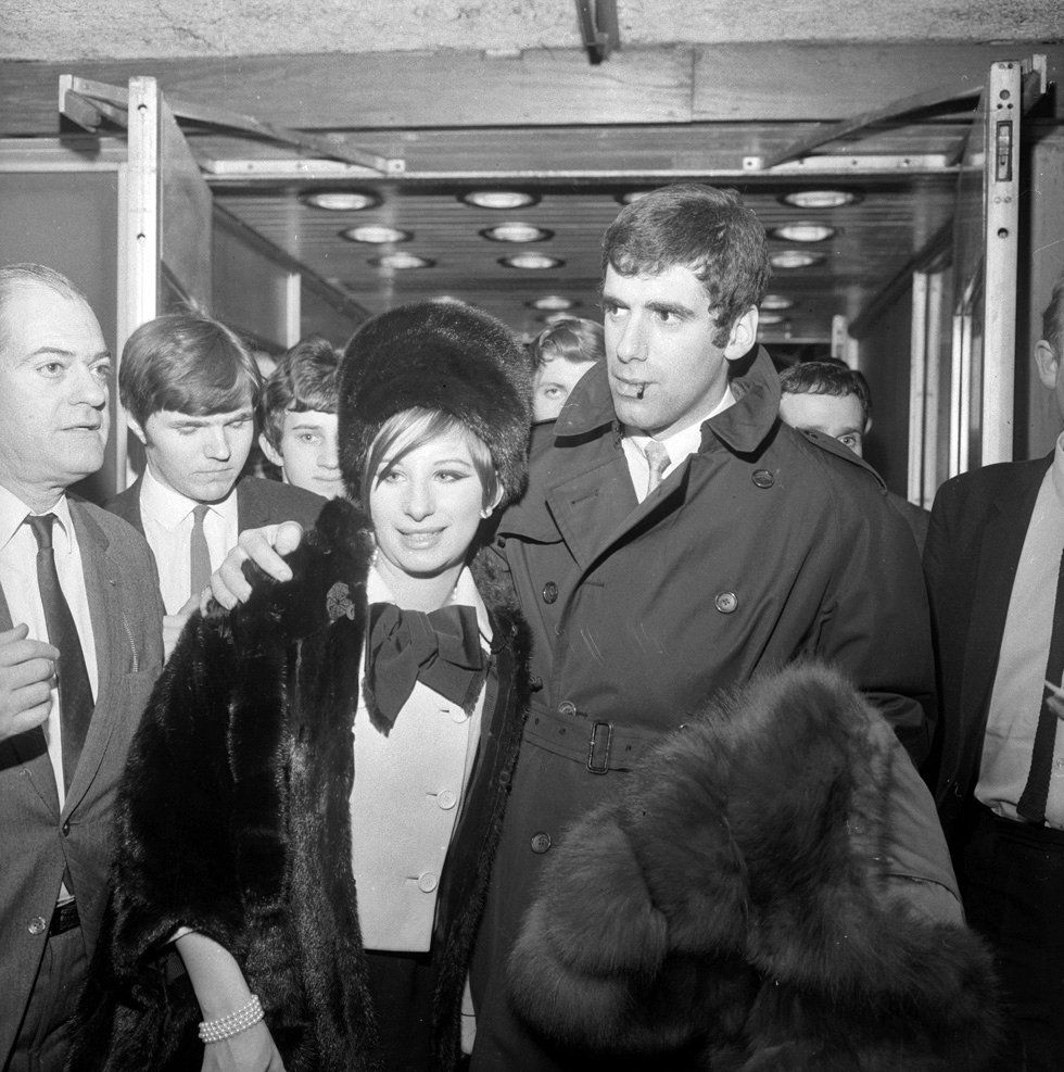 March 17, 1966 Streisand and Elliott Gould are welcomed by photographers when they arrive at Heathrow Airport.