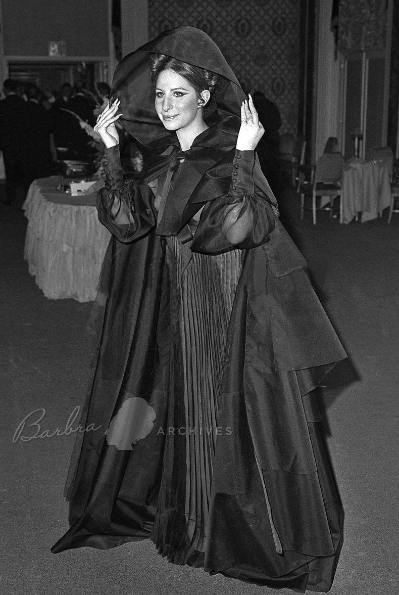 Streisand wearing black organza Dior gown with a hooded cloak.