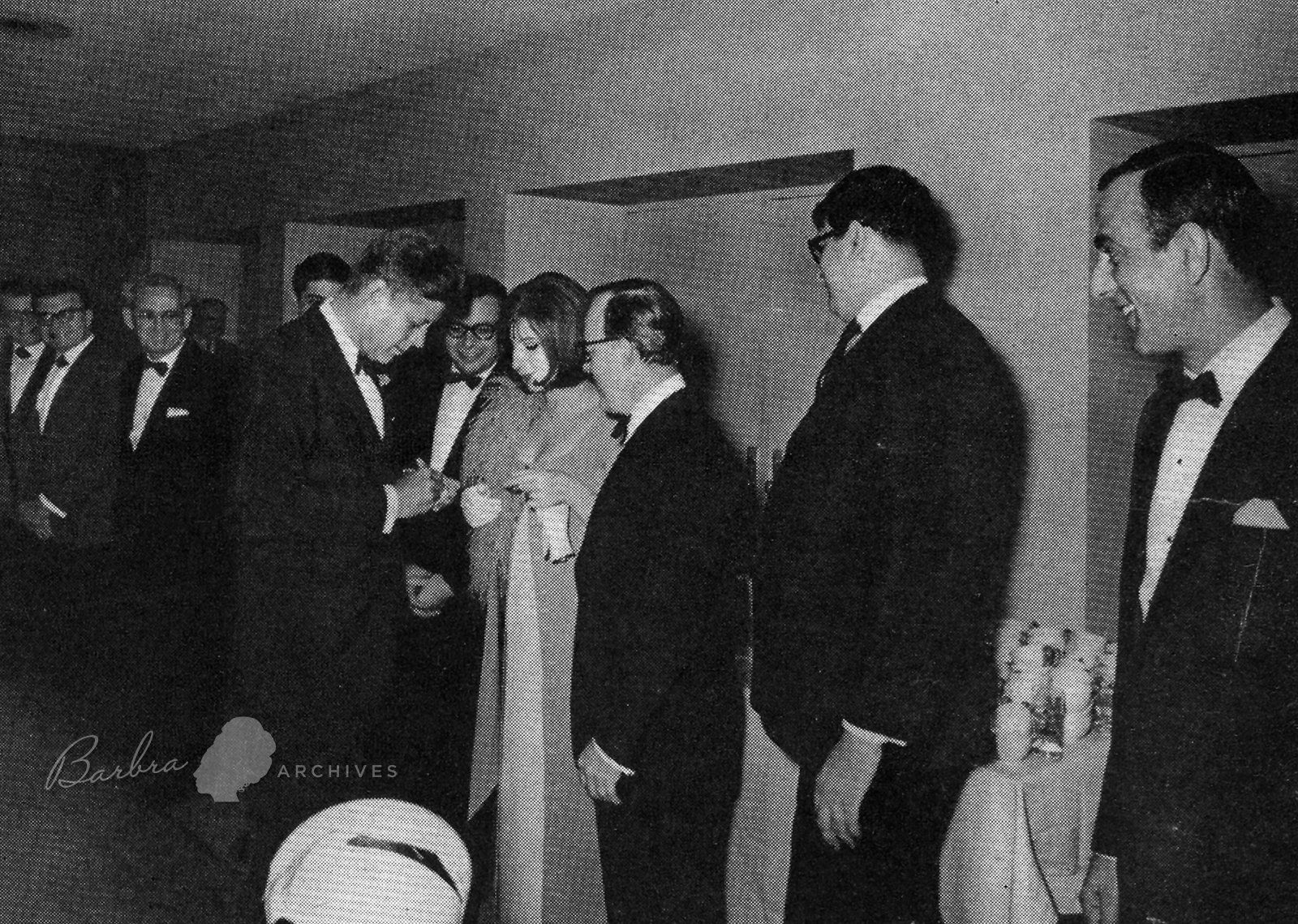 Streisand gets President Kennedy to sign his autograph as manager Marty Erlichman looks on.