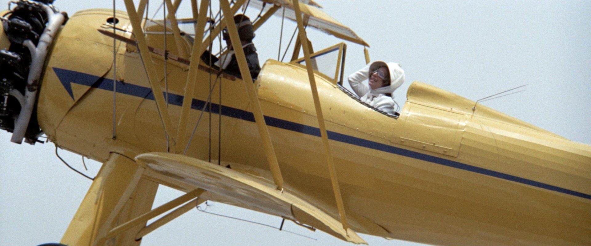 Streisand singing in the air in a yellow, open cockpit plane.
