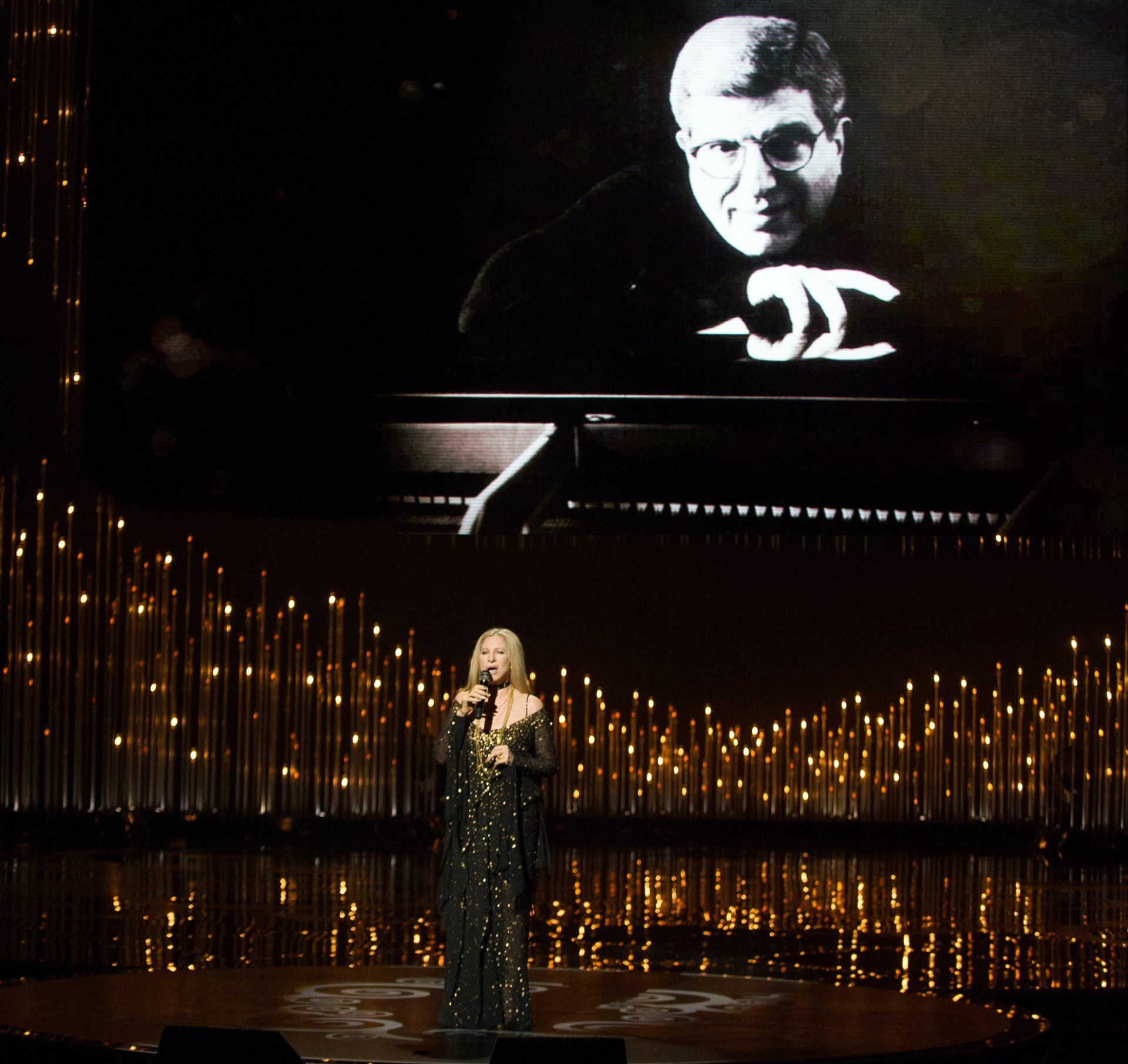 Streisand sings with Hamlisch on screen behind her.