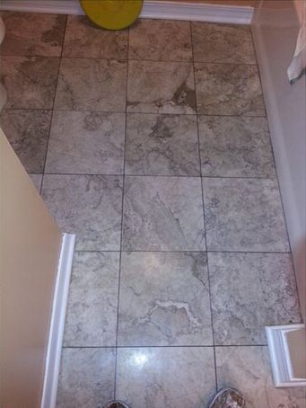 A bathroom with a tiled floor and a yellow bucket on the floor.