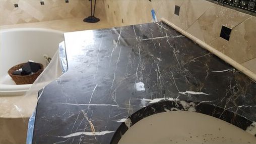 A bathroom with a black marble counter top and a bathtub.